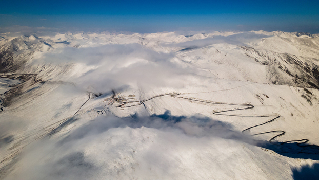 Aerial view of Babusar Pass with its winding road snaking through snow covered mountain peaks under a clear blue sky and soft clouds in Babusar KPK Pakistan. Aerial view of Babusar Pass with its winding road snaking through snow covered mountain peaks under a clear blue sky and soft clouds in Babusar KPK Pakistan.