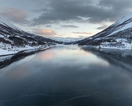 Aerial view of a frozen fjord surrounded by snow covered mountains under a soft twilight sky in Tromso Troms Norway. Aerial view of a frozen fjord surrounded by snow covered mountains under a soft twilight sky in Tromso Troms Norway.