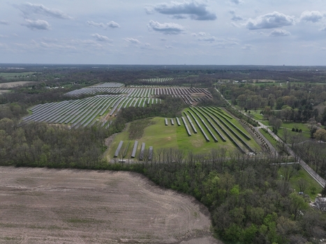 Lebanon United States 12 April 2026 Aerial view of a large solar farm with rows of photovoltaic panels surrounded by dense green forests and open fields under a cloudy sky.