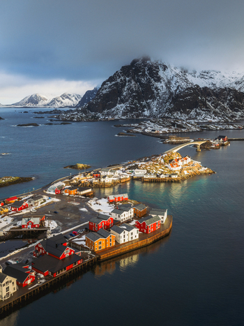 Aerial view of the vibrant red and white buildings contrasting against the deep blue sea and snow capped mountains of Henningsv&aelig;r Nordland Norway.
