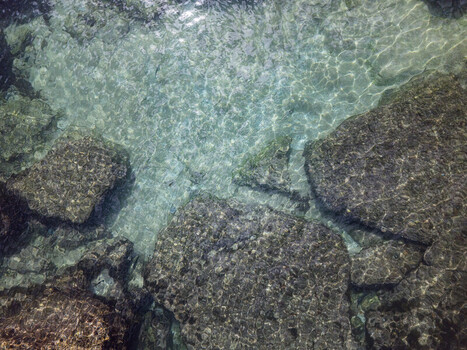 Aerial view of clear turquoise water over submerged dark rocks with sunlight reflections Cascais Lisbon Portugal. Aerial view of clear turquoise water over submerged dark rocks with sunlight reflections Cascais Lisbon Portugal.