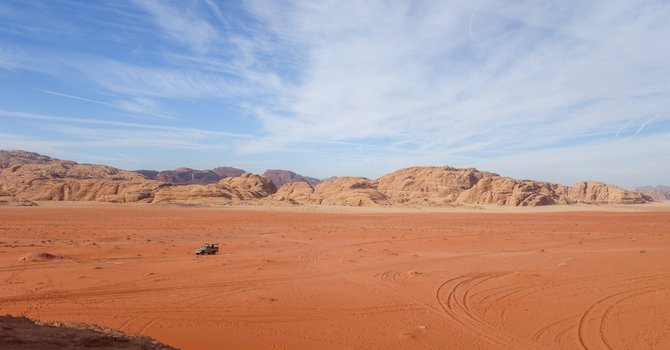 View of Wadi Rum Desert with red sand dunes rocky mountains and a 4x4 vehicle driving across the vast landscape in Wadi Rum Village Aqaba Governorate Jordan. View of Wadi Rum Desert with red sand dunes rocky mountains and a 4x4 vehicle driving across the vast landscape in Wadi Rum Village Aqaba Governorate Jordan.