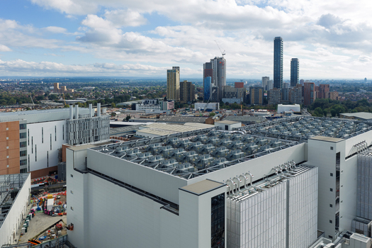 Aerial view of a large data center facility with cooling units on the roof situated in an urban area with a modern city skyline in the background United Kingdom. Aerial view of a large data center facility with cooling units on the roof situated in an urban area with a modern city skyline in the background United Kingdom.