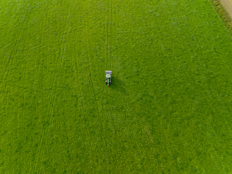Aerial view of a green tractor working in a large vibrant green field with visible tire tracks in Looe Cornwall United Kingdom. Aerial view of a green tractor working in a large vibrant green field with visible tire tracks in Looe Cornwall United Kingdom.