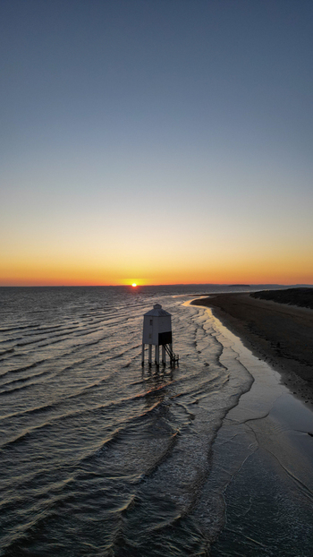 Aerial view of the iconic Burnham on Sea Low Lighthouse on stilts on the sandy beach during a golden sunset with gentle waves washing the shore in Burnham on Sea England United Kingdom. Aerial view of the iconic Burnham on Sea Low Lighthouse on stilts on the sandy beach during a golden sunset with gentle waves washing the shore in Burnham on Sea England United Kingdom.
