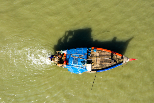Aerial view of a traditional wooden fishing boat carrying fishermen across the calm waters of the Bay of Bengal near Kuakata Barisal Division Bangladesh. Aerial view of a traditional wooden fishing boat carrying fishermen across the calm waters of the Bay of Bengal near Kuakata Barisal Division Bangladesh.