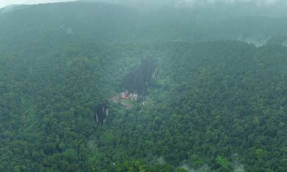 Aerial view of Yana Caves massive black limestone rock formations rising from the dense green forest under a misty sky in Yana Karnataka India.