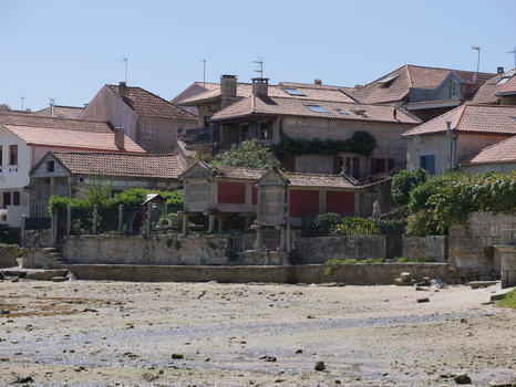 View of traditional stone horreos granaries situated along the waterfront with historic stone houses and terracotta rooftops in Combarro Pontevedra Spain.