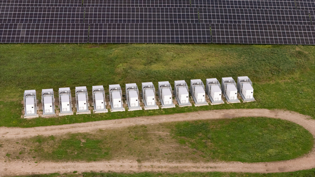 Aerial view of BESS battery energy storage system units installed in a row next to a large solar panel farm in Poland. Aerial view of BESS battery energy storage system units installed in a row next to a large solar panel farm in Poland.