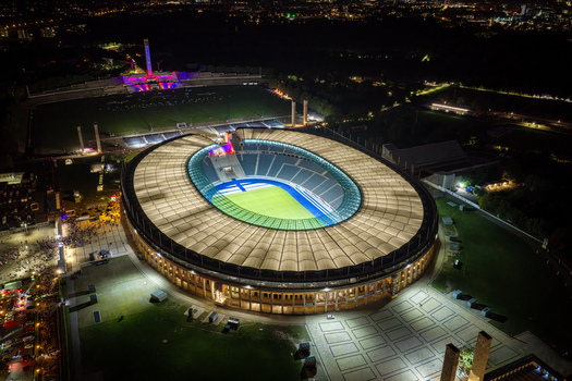 Berlin Germany 26 September 2026 Aerial view of Olympiastadion Berlin illuminated at night showing its oval architecture expansive roof and vibrant green pitch under stadium lights.
