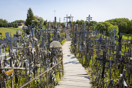 View of the Hill of Crosses featuring thousands of wooden and metal crosses along a central walkway under a clear blue sky in Siauliai Siauliu apskritis Lithuania. View of the Hill of Crosses featuring thousands of wooden and metal crosses along a central walkway under a clear blue sky in Siauliai Siauliu apskritis Lithuania.