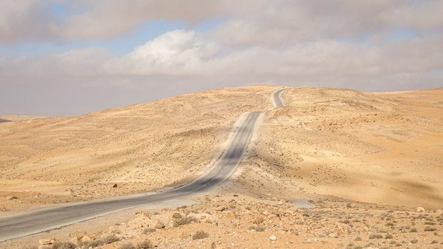 View of Wadi Rum Desert with a winding asphalt road cutting through the vast arid landscape under a partly cloudy sky in Wadi Rum Village Aqaba Governorate Jordan. View of Wadi Rum Desert with a winding asphalt road cutting through the vast arid landscape under a partly cloudy sky in Wadi Rum Village Aqaba Governorate Jordan.