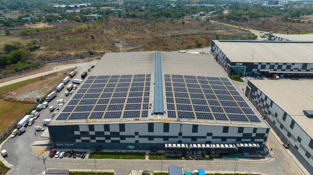 Aerial view of a large warehouse building featuring extensive rooftop solar panels with numerous trucks parked in the loading area in Bhiwandi Maharashtra India. Aerial view of a large warehouse building featuring extensive rooftop solar panels with numerous trucks parked in the loading area in Bhiwandi Maharashtra India.