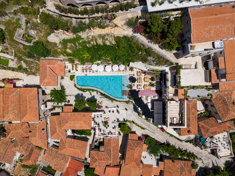 Aerial view of a luxury resort swimming pool surrounded by traditional red tiled rooftops and white sun umbrellas in Dhermi Vlore County Albania.