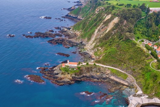 Aerial view of Cudillero Lighthouse on a rocky cliff overlooking the blue Cantabrian Sea with lush green hills in Cudillero Asturias Spain. Aerial view of Cudillero Lighthouse on a rocky cliff overlooking the blue Cantabrian Sea with lush green hills in Cudillero Asturias Spain.