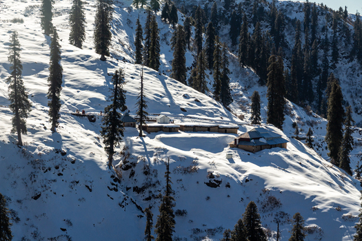 View of snow blanketed slopes dotted with evergreen trees and humble dwellings a serene winter scene unfolds in Lasdana Azad Kashmir Pakistan.