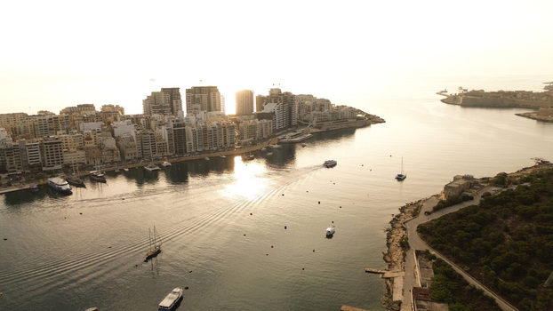 Aerial view of the coastal cityscape of Sliema and Gzira featuring modern apartment buildings and boats anchored in the harbor during golden hour in Malta. Aerial view of the coastal cityscape of Sliema and Gzira featuring modern apartment buildings and boats anchored in the harbor during golden hour in Malta.