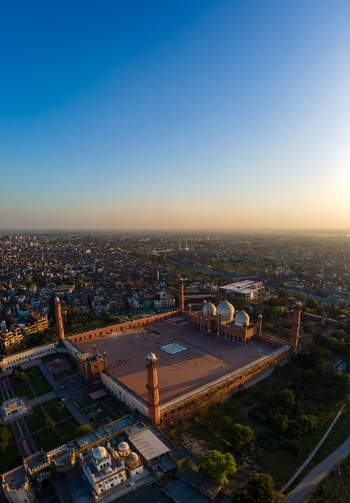 Aerial view of the historic Badshahi Mosque with its iconic red sandstone minarets and expansive courtyard set against the dense urban landscape of Lahore Punjab Pakistan. Aerial view of the historic Badshahi Mosque with its iconic red sandstone minarets and expansive courtyard set against the dense urban landscape of Lahore Punjab Pakistan.
