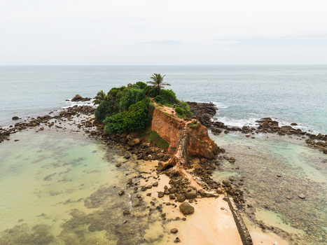 Aerial view of Parrot Rock with people walking on the path amidst lush greenery and turquoise waters in Mirissa Southern Province Sri Lanka. Aerial view of Parrot Rock with people walking on the path amidst lush greenery and turquoise waters in Mirissa Southern Province Sri Lanka.
