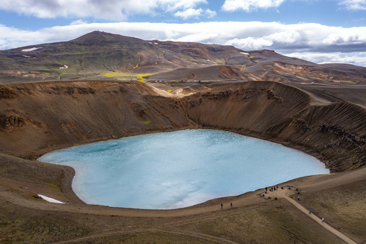 Aerial view of Viti crater lake at Krafla volcanic caldera with turquoise water rugged brown volcanic slopes and walking paths in Thingeyjarsveit Iceland.