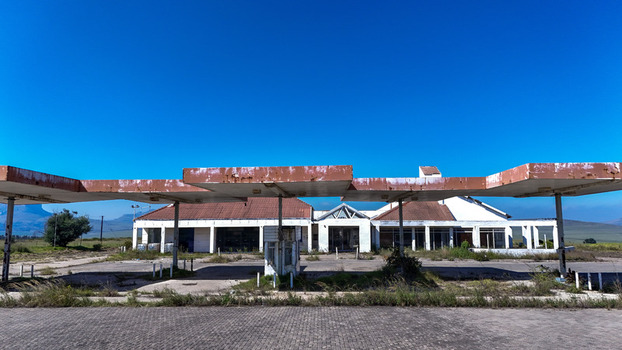 Aerial view of an abandoned gas station with a rusty canopy and white building under a clear blue sky in iNtabazwe Free State South Africa. Aerial view of an abandoned gas station with a rusty canopy and white building under a clear blue sky in iNtabazwe Free State South Africa.