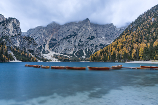 View of wooden rowing boats floating on the turquoise waters of Pragser Wildsee surrounded by autumn forests and misty mountains in Prags Trentino Alto Adige Italy.