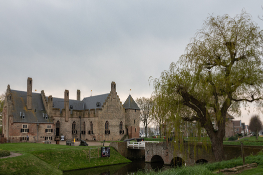 View of Radboud Castle with its medieval brick walls a stone bridge over the moat and a large willow tree under a cloudy sky in Medemblik Noord Holland Netherlands. View of Radboud Castle with its medieval brick walls a stone bridge over the moat and a large willow tree under a cloudy sky in Medemblik Noord Holland Netherlands.