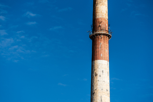 View of a tall industrial chimney with weathered red and white paint and communication antennas against a clear blue sky in Poland.