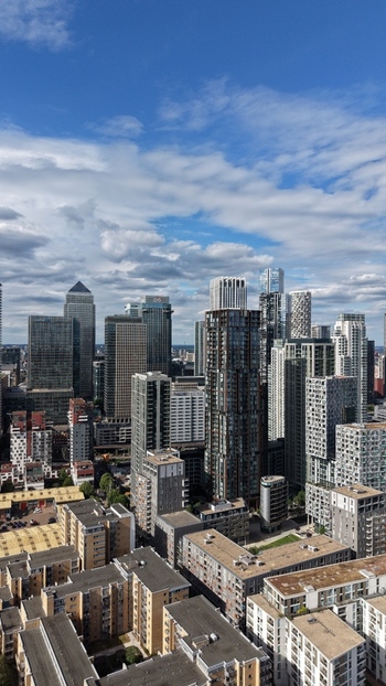 London United Kingdom 16 June 2026 Aerial view of the modern skyscrapers of Canary Wharf financial district with dense residential apartment blocks and a blue cloudy sky.