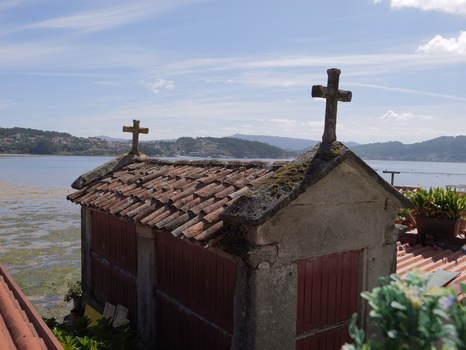 View of a traditional stone horreo with crosses on its tiled roof overlooking the estuary in Combarro Pontevedra Spain.