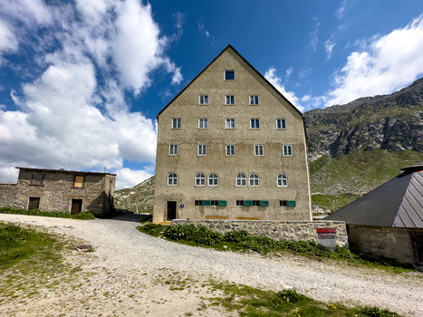 View of the historic Sankt Gotthard Pass building with its distinctive triangular roof under a blue sky with clouds in Airolo Ticino Switzerland.