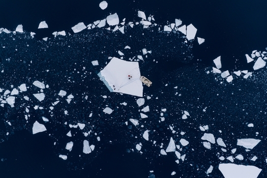 Aerial view of a small boat moored to a large flat iceberg with people standing on it in the dark arctic waters Tasiilaq Sermersooq Municipality Greenland. Aerial view of a small boat moored to a large flat iceberg with people standing on it in the dark arctic waters Tasiilaq Sermersooq Municipality Greenland.
