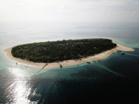Aerial view of a lush tropical island surrounded by turquoise waters sandy beaches and small wooden boats anchored near the shore in Sumenep East Java Indonesia.