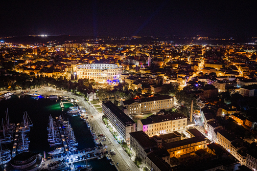 Aerial view of the illuminated Pula Arena amphitheater at night surrounded by the historic city lights harbor and boats in Pula Istria County Croatia. Aerial view of the illuminated Pula Arena amphitheater at night surrounded by the historic city lights harbor and boats in Pula Istria County Croatia.