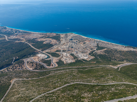 Aerial view of the winding roads of Llogara Pass featuring coastal development rugged mountain terrain and the deep blue Ionian Sea in Llogara Vlore County Albania. Aerial view of the winding roads of Llogara Pass featuring coastal development rugged mountain terrain and the deep blue Ionian Sea in Llogara Vlore County Albania.