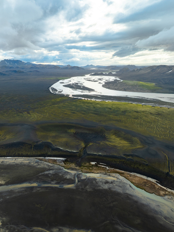 Aerial view of the volcanic landscape of Landmannalaugar with its braided river winding through mossy green hills and dark terrain under a dramatic cloudy sky in Rangarthing ytra Iceland. Aerial view of the volcanic landscape of Landmannalaugar with its braided river winding through mossy green hills and dark terrain under a dramatic cloudy sky in Rangarthing ytra Iceland.