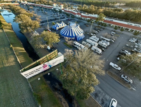 Aerial view of a vibrant blue and white striped circus tent nestled in a parking lot beside a canal framed by a billboard and retail stores St. Augustine Florida United States. Aerial view of a vibrant blue and white striped circus tent nestled in a parking lot beside a canal framed by a billboard and retail stores St. Augustine Florida United States.