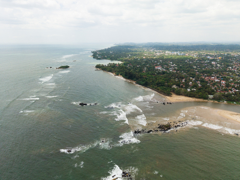 Aerial view of the coastline with waves crashing on rocks and lush green vegetation along the sandy beach in Matara Southern Province Sri Lanka. Aerial view of the coastline with waves crashing on rocks and lush green vegetation along the sandy beach in Matara Southern Province Sri Lanka.