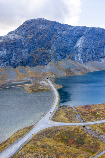 Aerial view of Skjakvegen road winding through a dramatic mountain landscape with a deep blue lake and rocky terrain in Skjak Innlandet Norway. Aerial view of Skjakvegen road winding through a dramatic mountain landscape with a deep blue lake and rocky terrain in Skjak Innlandet Norway.