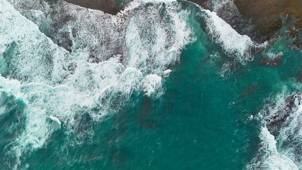 Aerial view of turquoise ocean waves crashing against the rocky coastline of Indonesia. Aerial view of turquoise ocean waves crashing against the rocky coastline of Indonesia.