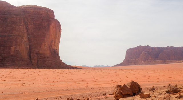 View of Wadi Rum Desert with towering red sandstone cliffs vast sandy plains and rocky terrain under a bright sky in Wadi Rum Village Aqaba Governorate Jordan. View of Wadi Rum Desert with towering red sandstone cliffs vast sandy plains and rocky terrain under a bright sky in Wadi Rum Village Aqaba Governorate Jordan.