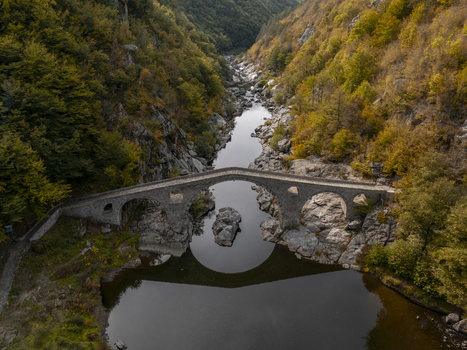 Aerial view of Devil s Bridge spanning the Arda River surrounded by lush autumn forests and rocky terrain in Kardzhali Province Bulgaria. Aerial view of Devil s Bridge spanning the Arda River surrounded by lush autumn forests and rocky terrain in Kardzhali Province Bulgaria.