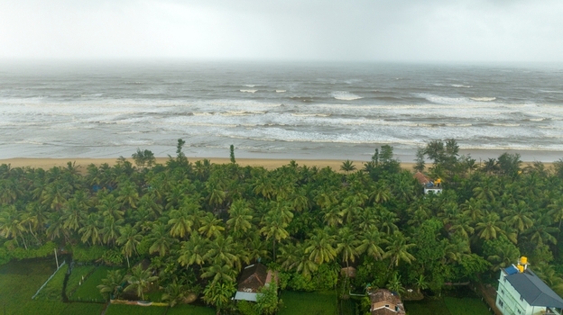 Aerial view of Gokarna beach with lush palm trees scattered houses and waves crashing on the sandy shore under a cloudy sky in Gokarna Karnataka India.