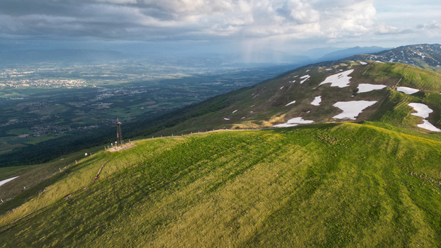 Aerial view of Le Colomby de Gex summit with green mountain ridges melting snow patches and the valley below under a dramatic cloudy sky Echenevex Auvergne Rhone Alpes France. Aerial view of Le Colomby de Gex summit with green mountain ridges melting snow patches and the valley below under a dramatic cloudy sky Echenevex Auvergne Rhone Alpes France.