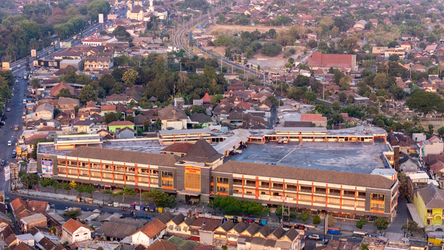 Indonesia 24 September 2026 Aerial view of a large market complex surrounded by dense urban rooftops lush trees and winding roads in Indonesia.