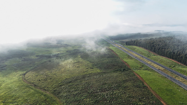 Aerial view of a highway cutting through green hills and forests partially covered by low clouds Garden Route District Municipality Western Cape South Africa.