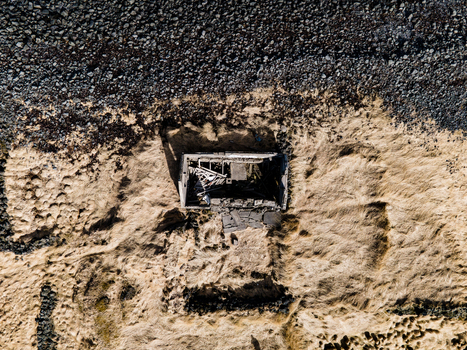 Aerial view of an abandoned farmhouse ruin surrounded by dry grass and dark volcanic rocks in Hafnarfjordur Hafnarfjardarkaupstad Iceland.