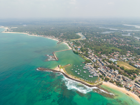 Aerial view of the harbor and coastline with fishing boats stone breakwaters and turquoise waters in Hikkaduwa Southern Province Sri Lanka. Aerial view of the harbor and coastline with fishing boats stone breakwaters and turquoise waters in Hikkaduwa Southern Province Sri Lanka.