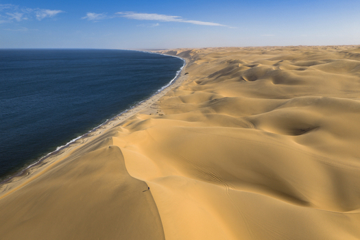 Aerial view of golden dunes meeting the dark blue ocean under a clear sky creating a stunning contrast of colors and textures Anichab Erongo Namibia. Aerial view of golden dunes meeting the dark blue ocean under a clear sky creating a stunning contrast of colors and textures Anichab Erongo Namibia.