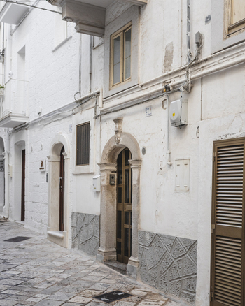 View of a narrow alley with traditional whitewashed stone buildings and arched doorways in the historic center of Polignano a Mare Apulia Italy.